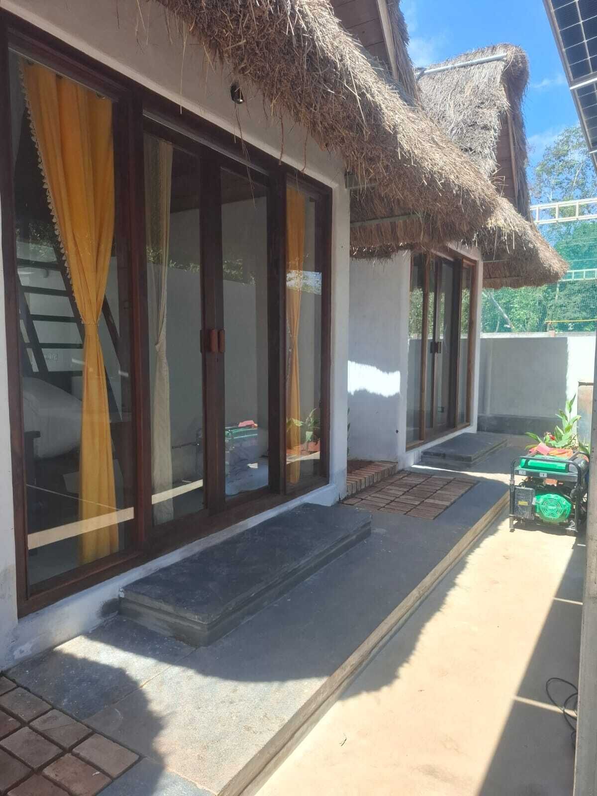 A building with large glass doors, a thatched roof, and a small outdoor area with a generator.