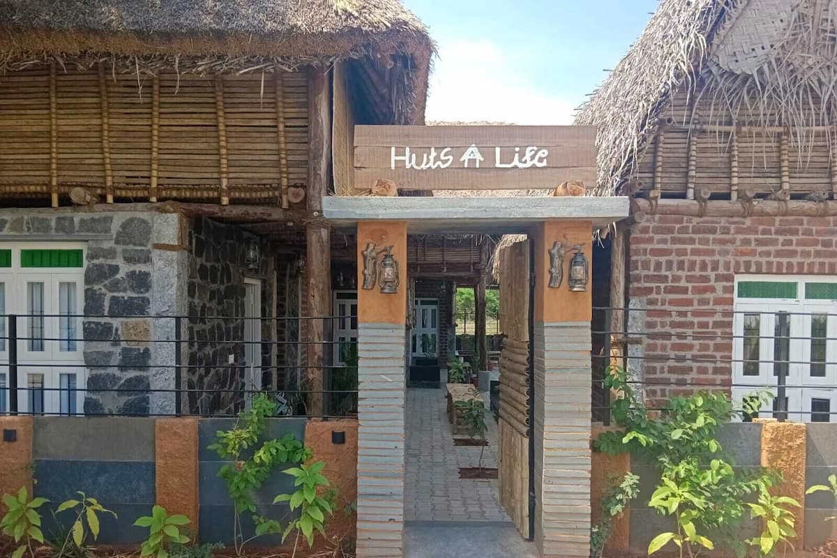 Un edificio con un letrero que dice 'Huts A Life', con techo de paja, paredes de piedra y una entrada pavimentada.