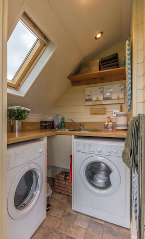 A compact laundry area with a skylight, a washing machine, a dryer, and a small sink.