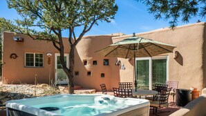 Un jacuzzi con mesa y sillas, una sombrilla y un árbol en un patio trasero.