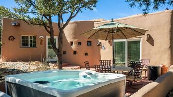 Un jacuzzi con mesa y sillas, una sombrilla y un árbol en un patio trasero.