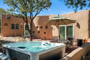 A hot tub with a table and chairs, a patio umbrella, and a tree in a backyard.