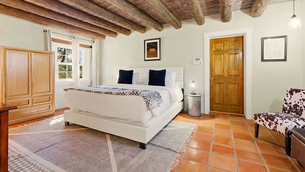 Un dormitorio con techo de madera, una cama con colcha estampada, una mesita de noche, una silla y una puerta.
