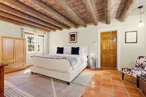 Un dormitorio con techo de madera, una cama con colcha estampada, una mesita de noche, una silla y una puerta.