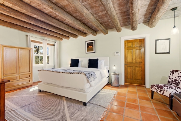 A bedroom with a wooden ceiling, a bed with a patterned bedspread, a nightstand, a chair, and a door.