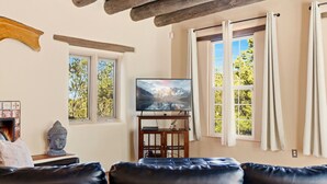 Una sala de estar con un sofá de cuero, un televisor sobre un mueble de madera y dos ventanas con cortinas.