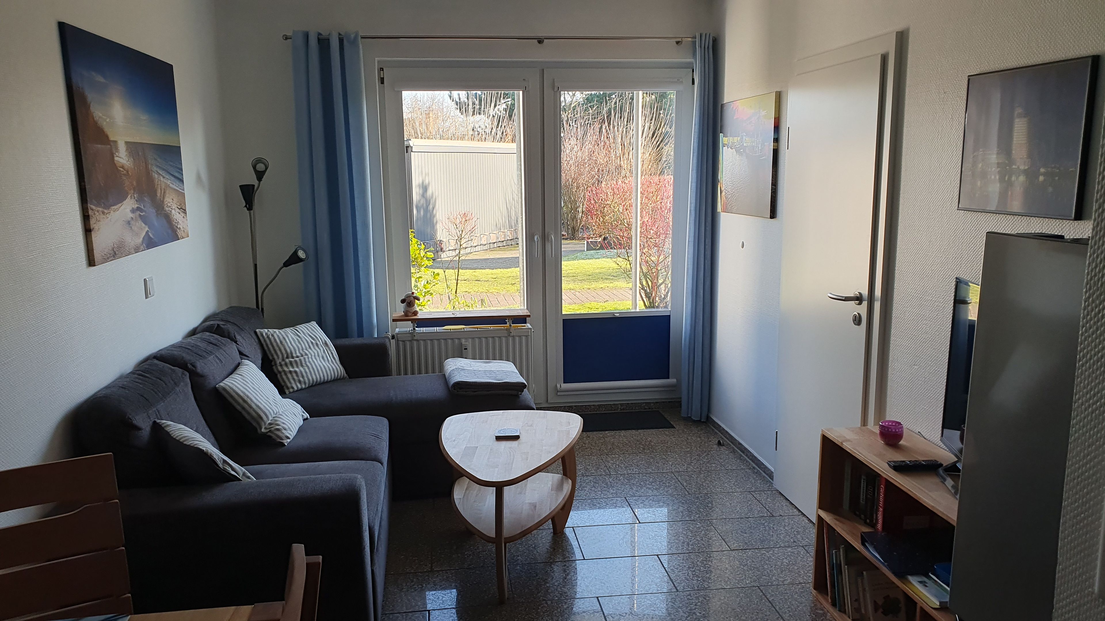 A living room with a sofa, a small table, a TV, and a view through a glass door.