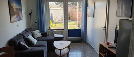 Una sala de estar con sofá, una mesita, televisor y vistas a través de un ventanal.