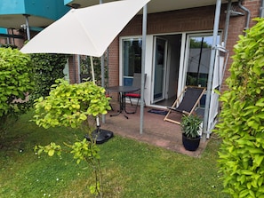 A patio area with a table, chairs, a white umbrella, and a glass door leading to a covered space.