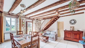 Un coin repas rustique avec des poutres apparentes, un escalier, un mur en pierre et une vue par la fenêtre.