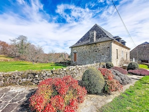 A stone building with a sloped roof, surrounded by a stone wall and a well-maintained garden with various plants. - Gîte Saint Sauveur by Interhome (St-Martin-La-Meanne)