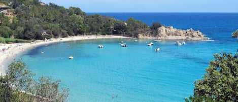 Uma praia costeira com águas azul-claras, barcos e areal arenoso.