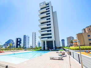 A modern building with a pool area, lounge chairs, and a clear sky. - Apartment Alexia by Interhome (Calpe/Calp)