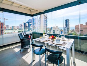 A dining area with a table set for two, a chair, and a view of a cityscape through large windows. - Apartment Alexia by Interhome (Calpe/Calp)