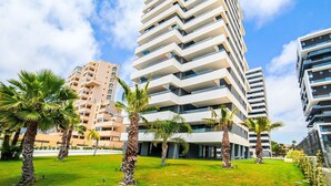 A modern high-rise building with multiple balconies, surrounded by palm trees and a well-maintained lawn. - Apartment Alexia by Interhome (Calpe/Calp)