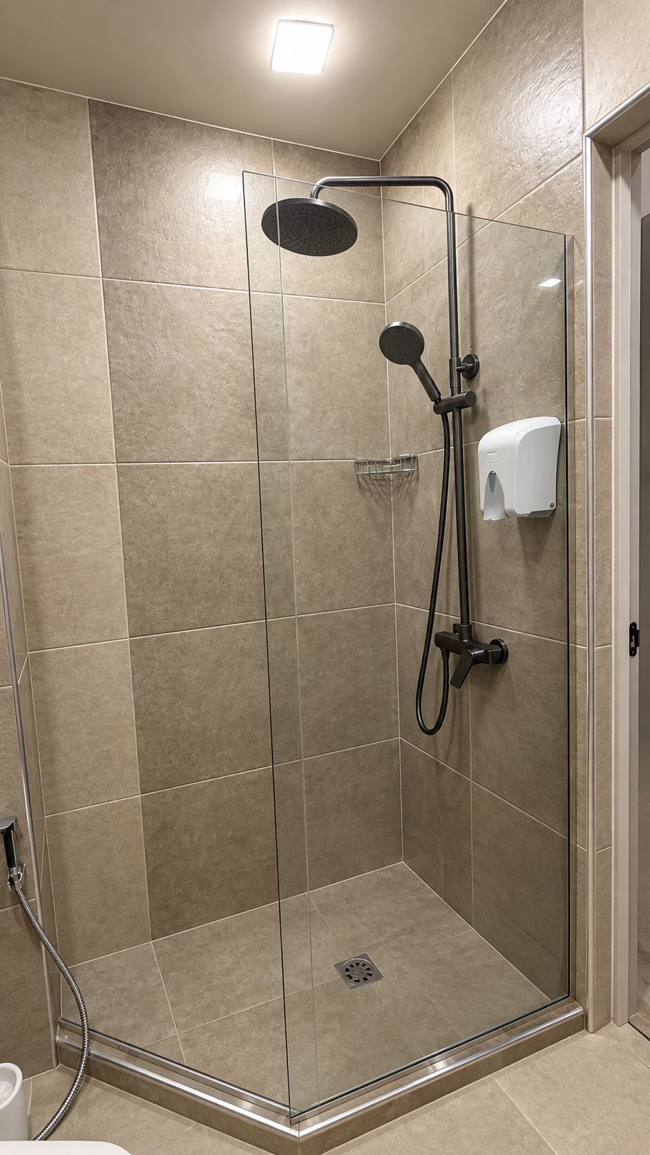 Une cabine de douche fermée par des parois en verre, équipée d’un pommeau de douche à main et d’un flexible de douche à main.