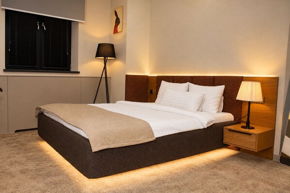 A hotel room with a bed, bedside table, lamp, and a window with blinds. - Fama 12 Hotel (Yerevan)