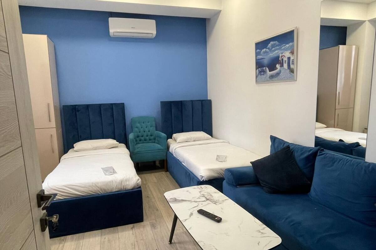 A room with two single beds, a blue sofa, a small table, and a teal armchair.