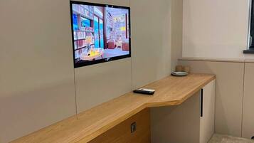 Una habitación moderna con un escritorio de madera, un televisor de pantalla plana en la pared y una ventana.