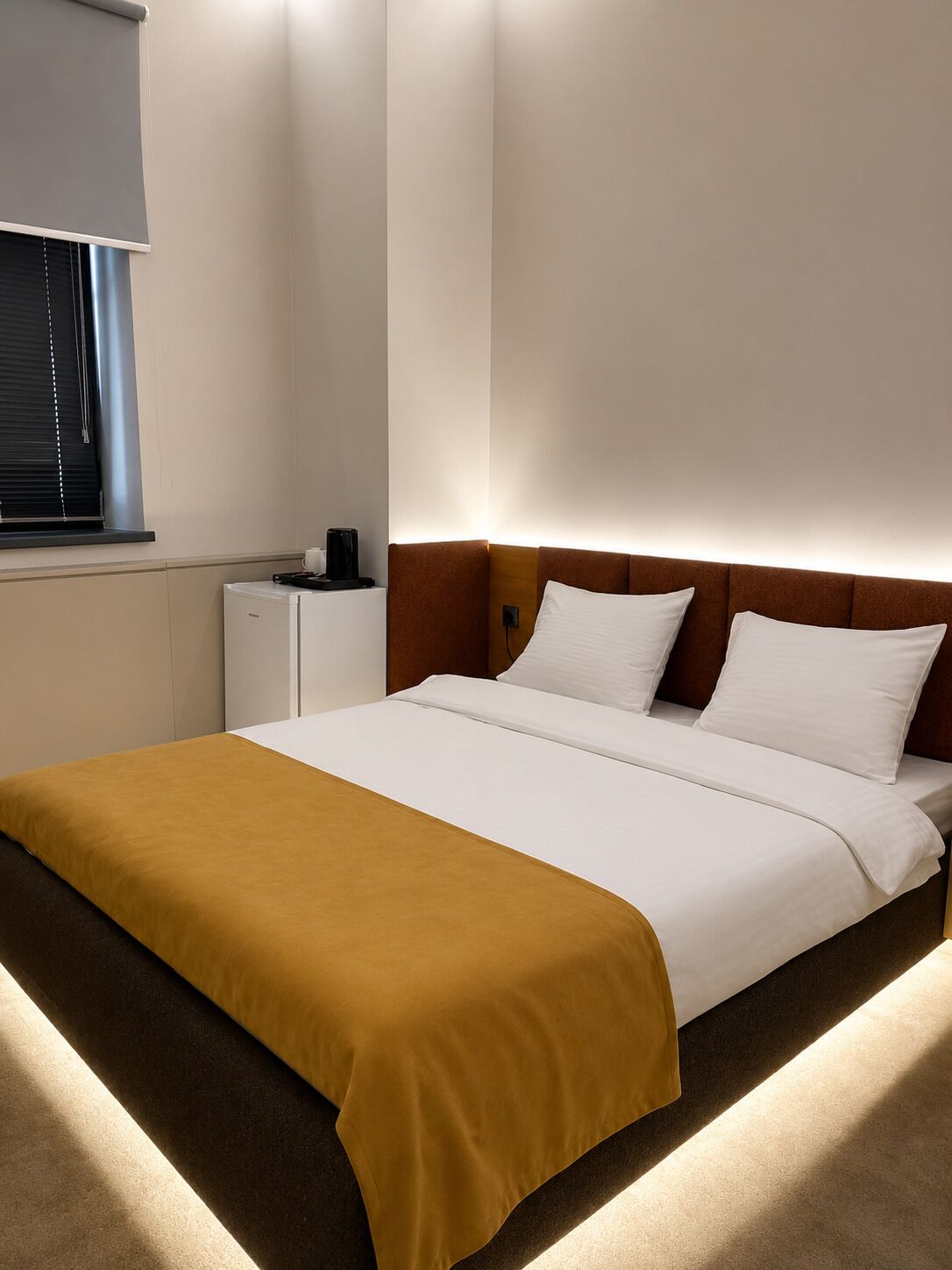 Une chambre d’hôtel avec un lit, une table de chevet, une lampe et une fenêtre avec des stores.