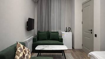 Un dormitorio moderno con un sofá verde, una cama blanca y una pequeña kitchenette.