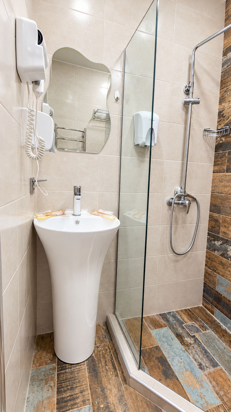 Un baño con un lavamanos blanco de pedestal, una cabina de ducha de vidrio y un secamanos montado en la pared.