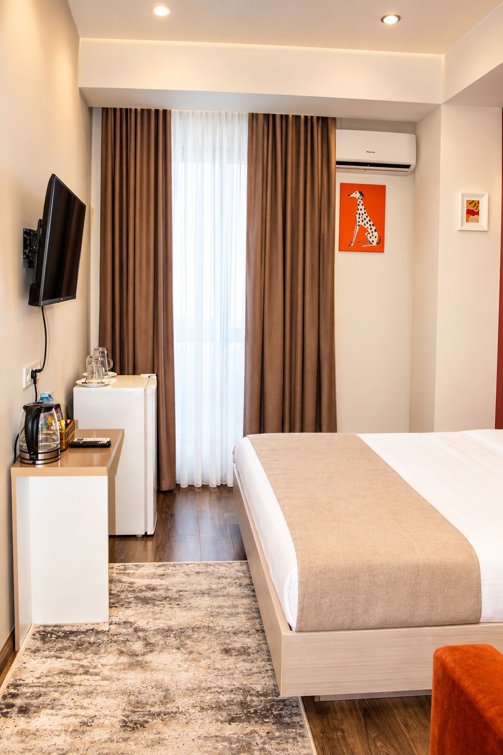 A hotel room with a bed, a desk, a television, and an air conditioning unit.