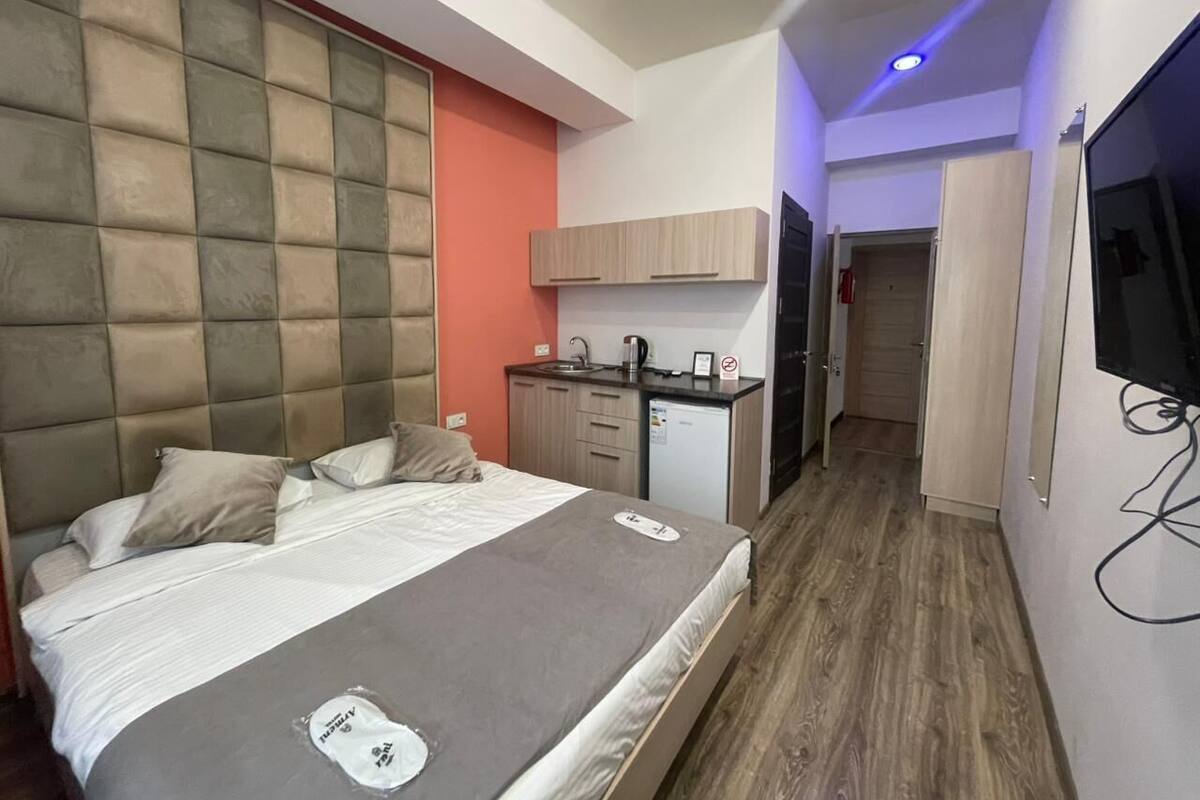 A hotel room with a bed, a desk, a small kitchenette, and a TV.