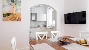Eine moderne Küche mit weißen Schränken, einem Esstisch mit weißen Stühlen und einem an der Wand befestigten Fernseher.