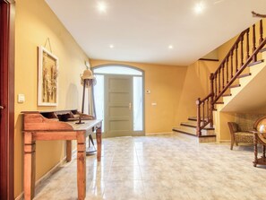 A spacious hallway with a wooden desk, a lamp, and a staircase leading to an upper level. - Ca l'Andreu by Interhome (Garriguella)