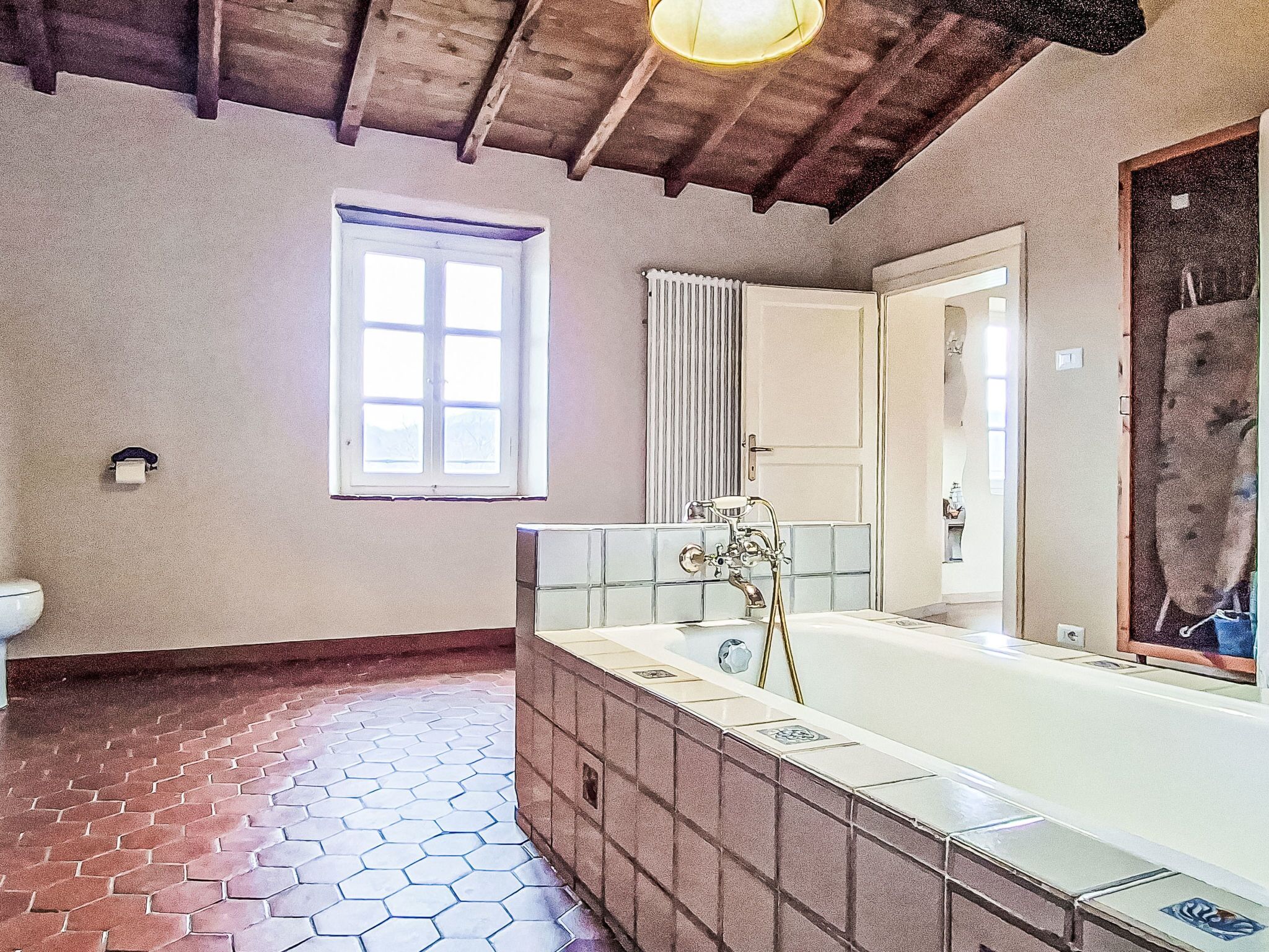 A bathroom with a large bathtub, a window, a toilet, and a tiled floor.