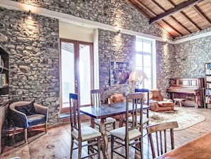 Una stanza con pareti in pietra, un tavolo da pranzo, sedie, un pianoforte e una libreria.