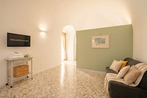 A room with a tiled floor, a sofa with cushions, a small table with a basket, a television, and a framed picture on the wall. - Auriga Elegance in Modugno (Modugno)