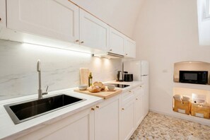 A kitchen with white cabinets, a black sink, a microwave, and a wooden cutting board with bread. - Auriga Elegance in Modugno (Modugno)