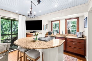 A modern kitchen with a large island, granite countertops, and a flat-screen TV. - Beach access, close to West Beach conference (Kiawah Island)