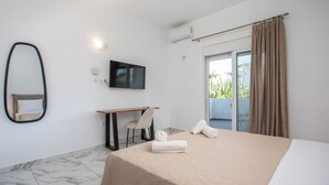 Habitació d'hotel amb llit, escriptori, cadira, televisió i balcó amb cortines.