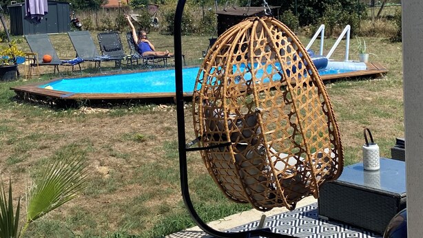Un área junto a la piscina con una hamaca colgante, sillas de descanso y una pequeña mesa.