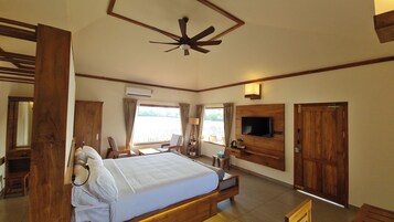 Una habitación de hotel con una cama, televisión, ventilador de techo, ventana con cortinas y una puerta de madera.