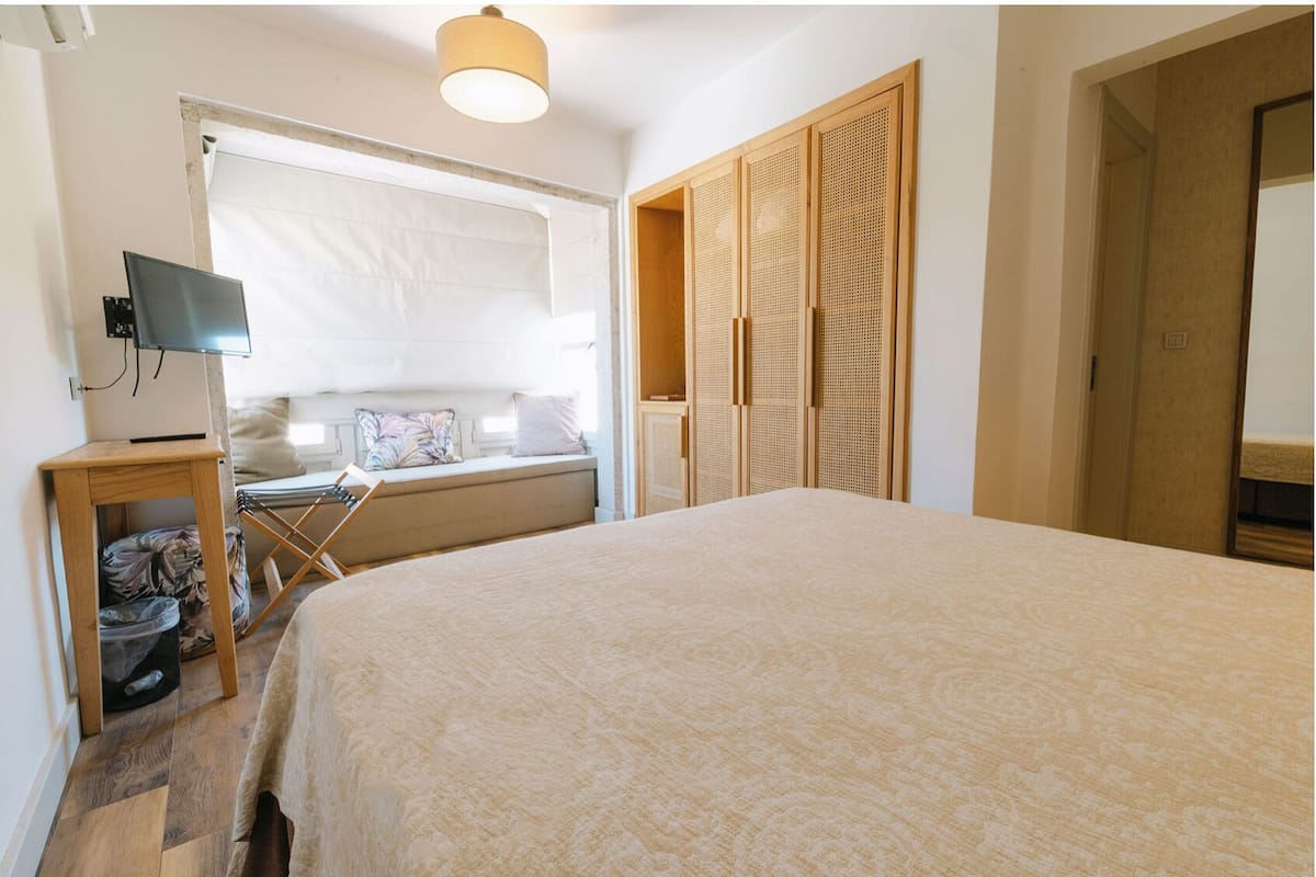 A bedroom with a bed, a television, a window, and a wardrobe.