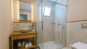 A bathroom with a glass-enclosed shower, a sink with a mirror above, and a shelf with towels. - Fiora Alacati Hotel (Çeşme)