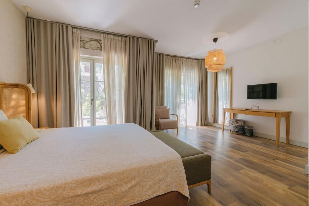 A bedroom with a large bed, a chair, a desk, a television, and a window with curtains.