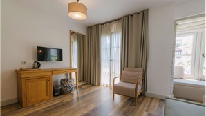 A room with a wooden desk, a chair, a television, a window with curtains, and a view outside. - Fiora Alacati Hotel (Çeşme)