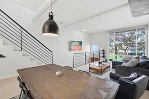 A modern living room with a dining table, sofa, and staircase.