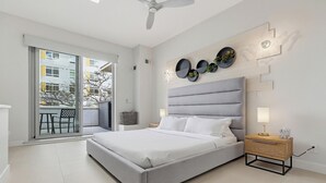 Un dormitorio moderno con una cama grande, una mesita de noche, una lámpara de pared y vistas a un balcón exterior por medio de puertas correderas.