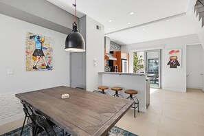 A modern kitchen with a dining area, a large wooden table, and bar stools.