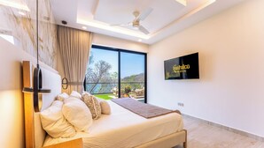 Un dormitorio moderno con una cama grande, ventilador de techo, televisor y vista al exterior.