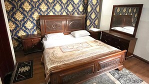 Een slaapkamer met een groot bed, nachtkastje, kapstok, spiegel en behang met dessin.