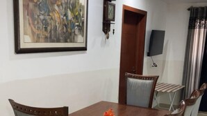 Een eetgedeelte met een houten tafel en zes stoelen, een schilderij aan de wand, een klok en een deur.