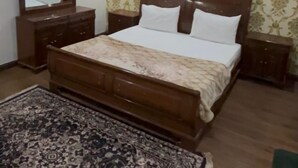 Een slaapkamer met een houten bed, een nachtkastje, een dressoir, een spiegel en een kamerkleed met dessin.