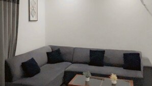 Een woonkamer met een grijze hoekbank, een houten salontafel en een kamerkleed met dessin.